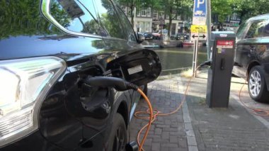 Amsterdam, Hollanda-05 Temmuz 2018: 4K. Amsterdam, Hollanda 'da bir kanalın yakınına park etmiş elektrikli bir arabayı şarj etmek. Çevre dostu alternatif enerji