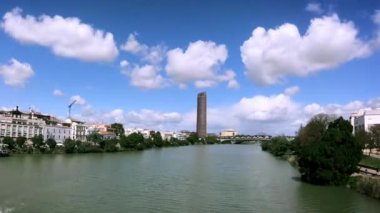 Torre Pelli ya da Torre Sevilla 'nın zamanı. Sevilla, İspanya' da ünlü bir gökdelen. Gualdalquivir nehri boyunca giden tekneler var. Güzel bulutlar. Kaydır, Hiperlapse