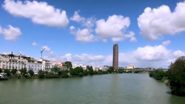 İspanya 'nın Sevilla şehrinin zamanı. Guadalquivir nehrinin üzerinde güzel bulutlar. Ufukta Sevilla Kulesi veya Pelli Kulesi görünüyor. Kaydır, Hiperlapse