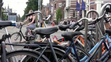 Amsterdam, Hollanda-06 Temmuz 2018: 4K. Amsterdam, Hollanda 'da bir caddeye park edilmiş bisikletler. Tramvay yaklaşıyor ve park edilmiş bisikletlerin arkasından geçiyor.