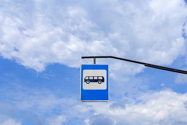Açık mavi bulutlu gökyüzünün arkaplanındaki otobüs durağı tabelası. Yukarıdan bir işaret. Üzerinde otobüs resmi olan mavi yol tabelası.