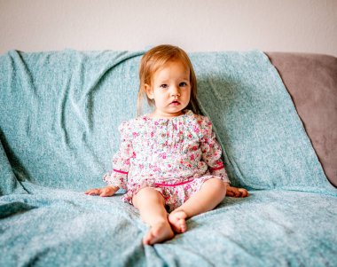 Sevimli bir bebek kız bir okyanus mavi sallama battaniye ile gri bir kanepede oturur.