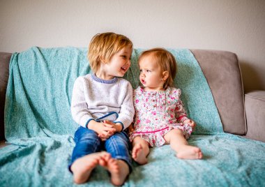 Genç bir erkek kardeşi ve kardeşi bir okyanus mavi sayıl battaniye ile gri bir kanepede oynamak. Kız çiçekli bir elbise giyerken çocuk mavi kot pantolon ve beyaz bir kazak giyiyor..