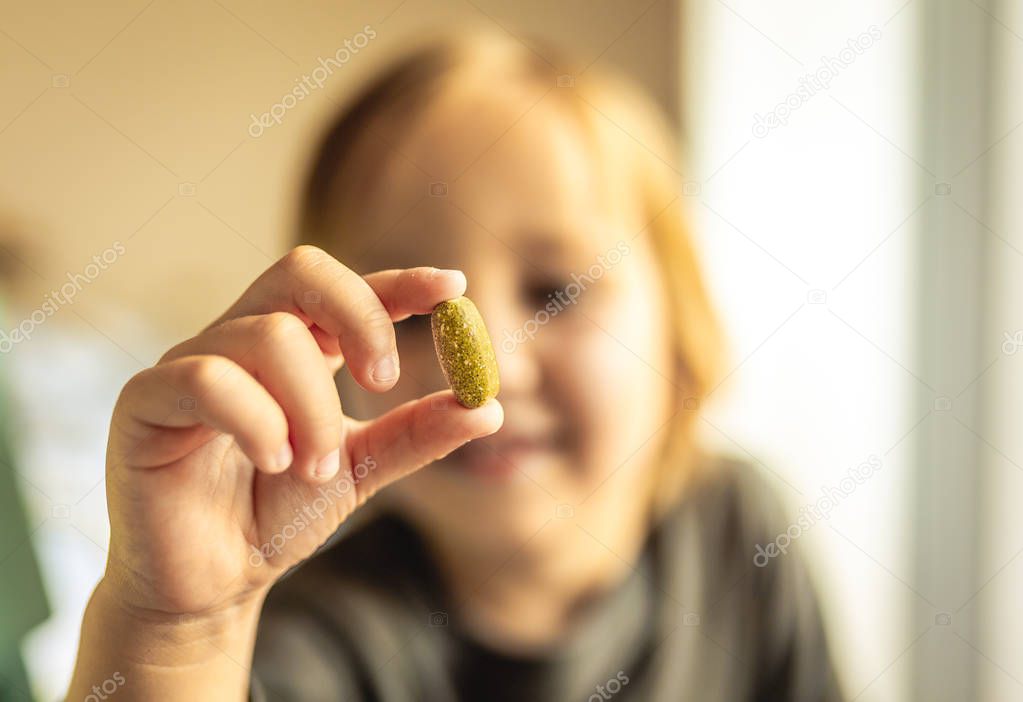 Young caucasian boy with blonde hair holds vitamin or prescription pill in hand. Health care concept. Medical concept. Addiction concept. Closeup.