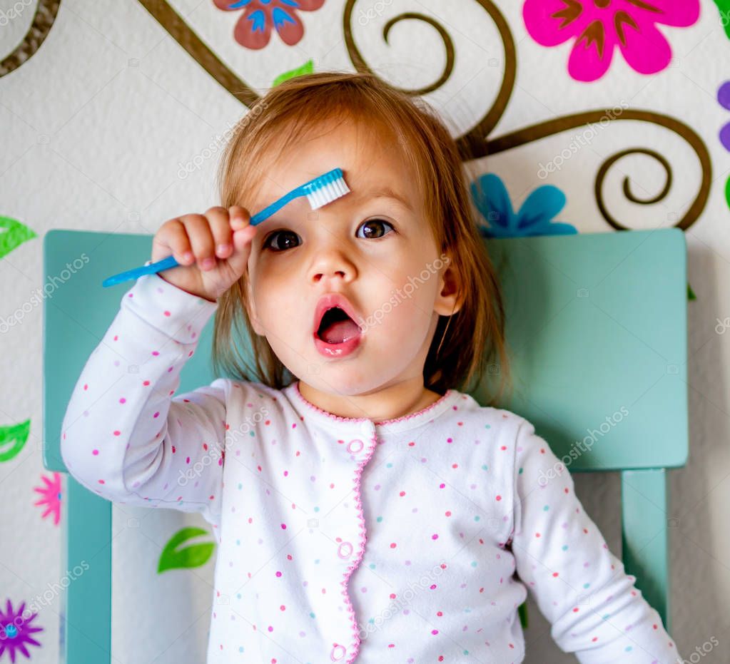 Adorable Toddler Girl Brushes Her Teeth in Pajamas. Health Care concept. Polka dot pajamas. Blue chair. Blue Toothbrush.