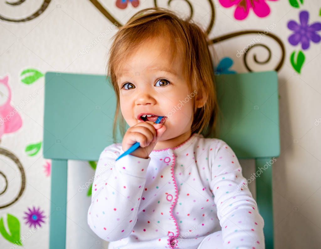 Adorable Toddler Girl Brushes Her Teeth in Pajamas. Health Care concept. Polka dot pajamas. Blue chair. Blue Toothbrush.
