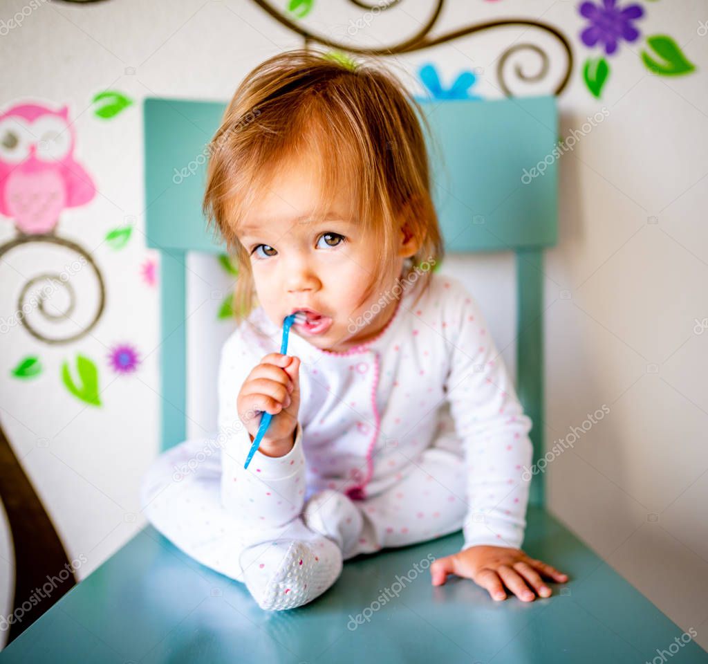 Adorable Toddler Girl Brushes Her Teeth in Pajamas. Health Care concept. Polka dot pajamas. Blue chair. Blue Toothbrush.