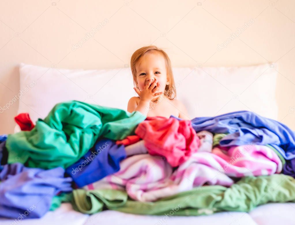 Cute, Adorable, Smiling, Caucasian Baby Sitting in a Pile of Dirty Laundry on Bed