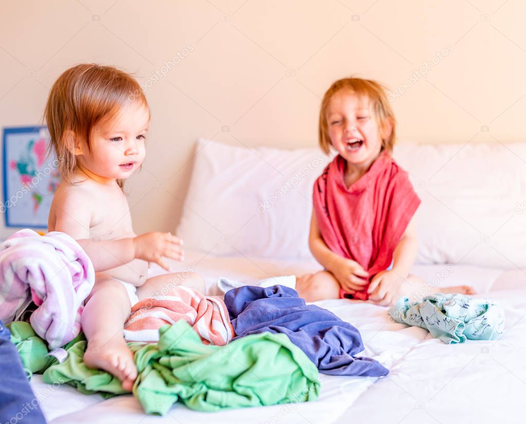 Mischievous Brother and Sister Play in a Pile of Laundry on the Bed. Family Concept. 