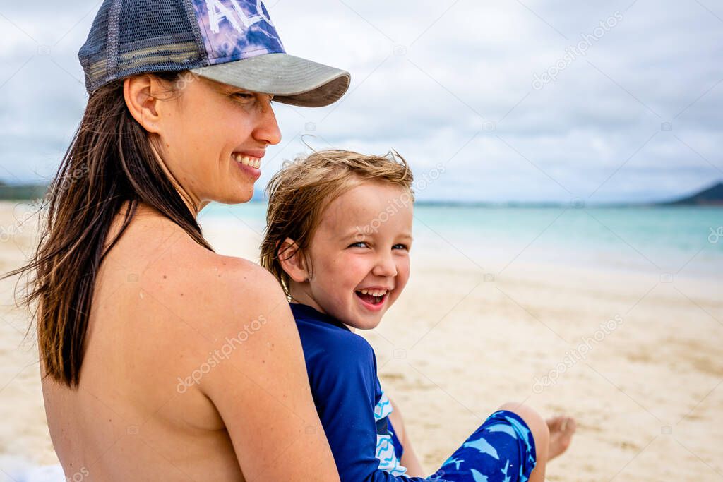 Mother and son sit on beach looking at the ocean