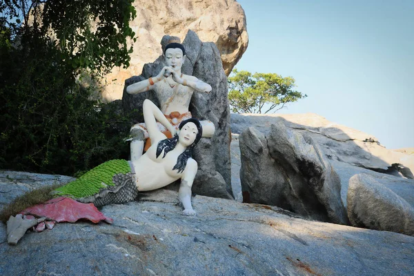 This unique nature picture shows a sculpture of a mermaid sitting on a rock and behind it a sculpture by a flute player who conjures it up.