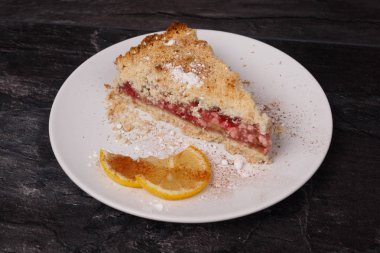 Kek ve limon beyaz bir tabakta, siyah bir arka planda.