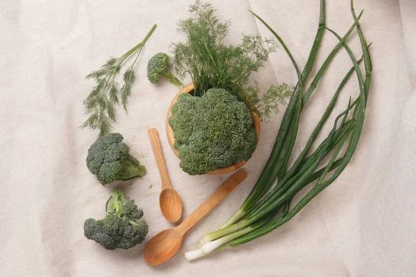 Groene uien, broccoli, dille in een houten kom en houten lepels — Stockfoto