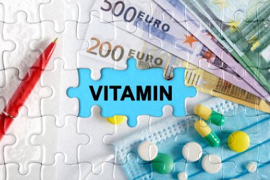 Çifte maruziyet. Üzerinde VITAMIN yazan hap, tıbbi maske, kalem ve avroyla bulmacalar. Tıp konsepti.