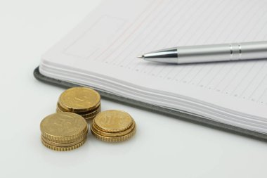 Bozuk paralar, boş not defteri ve beyaz arka planda bir kalem. İş ve teknoloji kavramı.