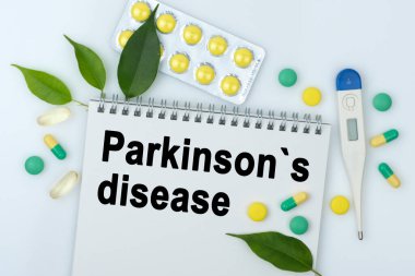 Masanın üzerinde haplar, bir termometre, yapraklar ve üzerinde Parkinson hastalığı yazan bir defter var. Tıp konsepti.