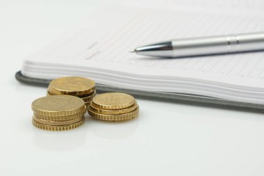 Bozuk paralar, boş not defteri ve beyaz arka planda bir kalem. İş ve teknoloji kavramı.