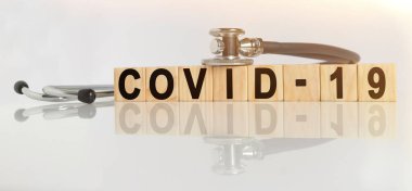 COVID-19. Tahta küplerde kullanılan sözcük, yansıtıcı beyaz bir yüzey, küpler üzerinde duran bir stetoskop. Tıp konsepti