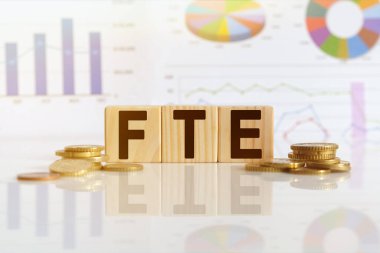 Tam zamanlı eşdeğer. Tahta küplerle ilgili kelime FTE, yansıtıcı bir yüzey üzerinde duran küpler, arka planda bir iş diyagramı var. İş ve finans kavramı