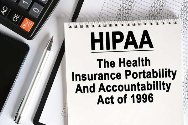 On the table lies a smartphone, a calculator and a notebook with the inscription- HIPAA. The Health Insurance Portability And Accountability Act of 1996. Business concept
