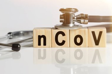 NCOV kelime ahşap küpler, küpler yansıtıcı beyaz bir yüzey üzerinde durur, küpler - stetoskop. Tıp konsepti
