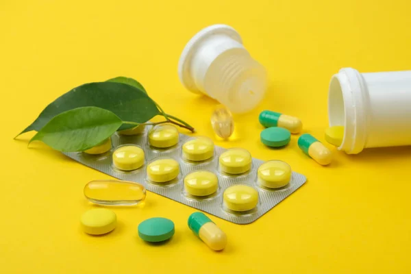 Yellow and green pills, jar and green leaves on a yellow background. Medicine concept