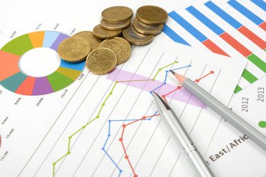 İş hedefi kavramı. İş aksesuarları, grafik çizelgeleri, kalemler ve madeni paralar masaya..