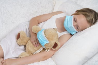 Hasta bir genç kız koruyucu maske takan bir oyuncakla oynuyor. Tıbbi konsept.