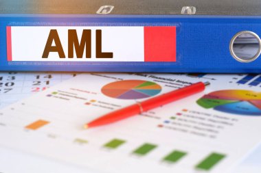 Masanın üzerinde pasta grafikleri, bir kalem ve üzerinde AML yazan bir klasör var. Kara para aklama karşıtı. İş ve finans kavramı.