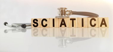 SCIATICA kelime ahşap küplerde, küpler yansıtıcı beyaz bir yüzey üzerinde durur, küplerde - bir stetoskop. Tıp konsepti