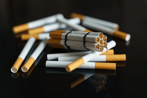 医学的概念是与吸烟作斗争 香烟以炸药棒的形式散落在黑色反光表面上的香烟中间 — 图库照片