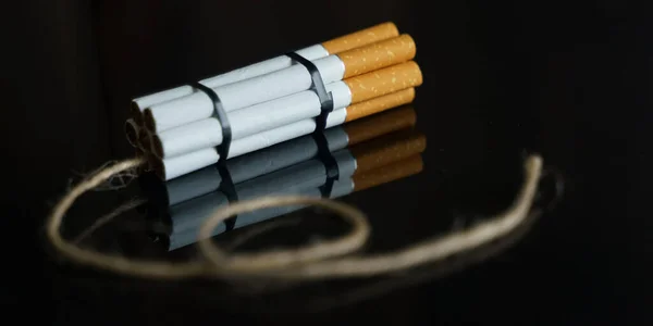 医学的概念是与吸烟作斗争 香烟被扭曲成在黑色反射面上有长丝的炸药止回阀 — 图库照片