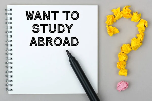 Hand with marker writing: Want to Study Abroad. Notepad and question mark.