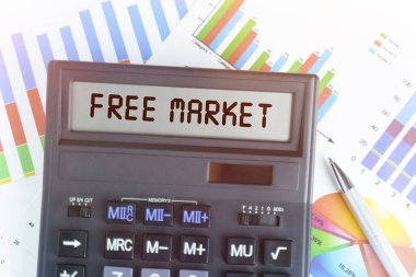 İş ve finans kavramı. Masanın üzerinde finansal tablolar ve bir hesap makinesi var, elektronik panoda metni yazılı - FREE MARKET