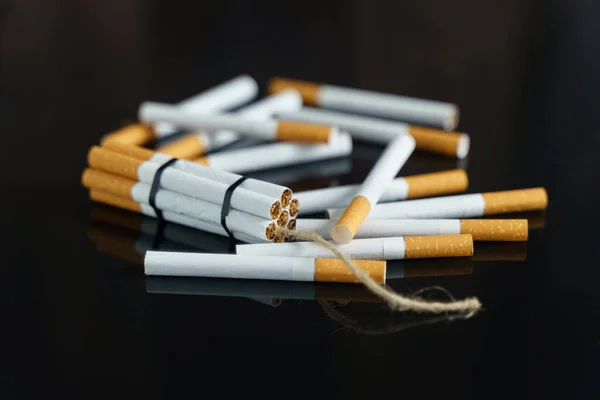 医学的概念是与吸烟作斗争 香烟以炸药棒的形式散落在黑色反光表面上的香烟中间 — 图库照片