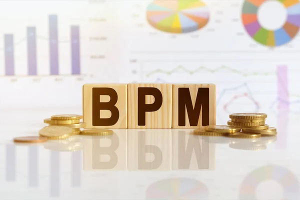 Business process management. BPM the word on wooden cubes, cubes stand on a reflective surface, in the background is a business diagram. Business and finance concept