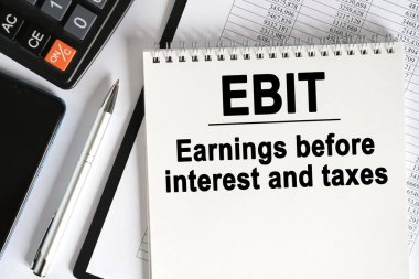 Masanın üzerinde bir akıllı telefon, bir hesap makinesi ve üzerinde EBIT yazan bir defter var. İş konsepti