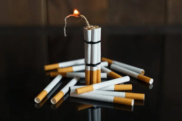 医学的概念是与吸烟作斗争 香烟的形式是带着燃烧芯的炸药棒 它们耸立在散落在黑色反光表面的香烟中间 — 图库照片