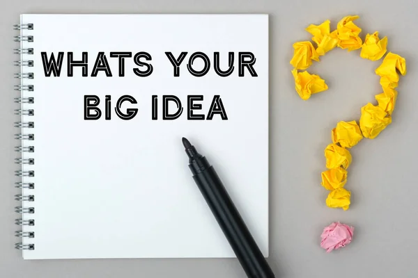 Hand with marker writing: Whats Your Big Idea. Notepad and question mark.