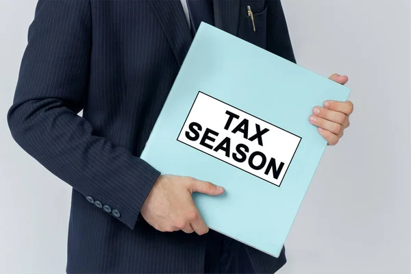 Business concept. A businessman holds a folder with documents, the text on the folder is - TAX SEASON