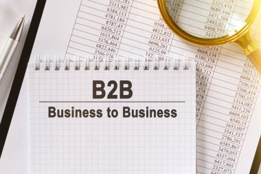 Masanın üzerinde mali raporlar, bir kalem, bir büyüteç ve üzerinde B2B yazan bir defter var. İşten işe. İş ve finans kavramı.