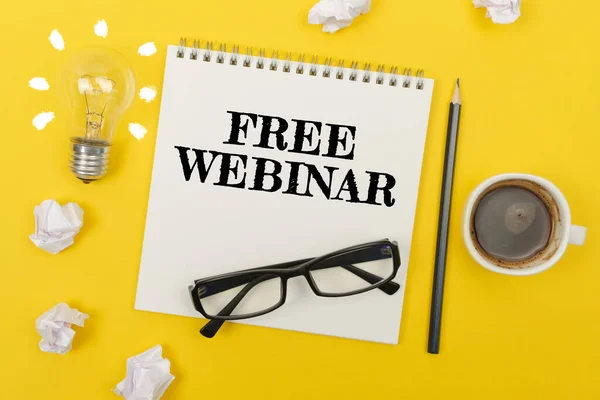 İş ve finans kavramı. Sarı masada: bir ampul - bir fikir, bir fincan kahve, bir parça kağıt, bardaklar ve yazılı bir defter - ücretsiz weBINAR