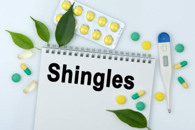 Masanın üzerinde haplar, bir termometre, yapraklar ve üzerinde yazı olan bir defter var. Tıp konsepti.