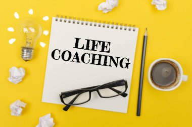 İş ve finans kavramı. Sarı masada: bir ampul - bir fikir, bir fincan kahve, bir parça kağıt, bardaklar ve yazılı bir defter - LIFE COACHING