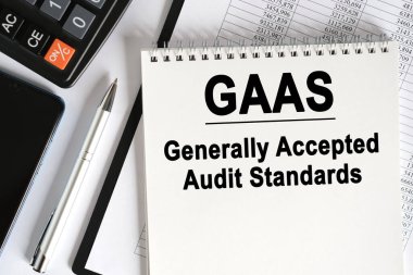 Masanın üzerinde bir akıllı telefon, bir hesap makinesi ve üzerinde GAAS yazan bir defter var. Genel olarak Kabul Edilen Denetim Standartları. İş konsepti