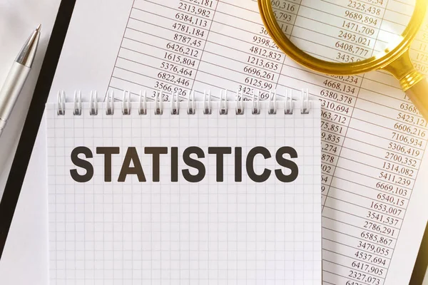 On the table are financial reports, a pen, a magnifying glass and a notebook with the inscription - STATISTICS. Business and finance concept.