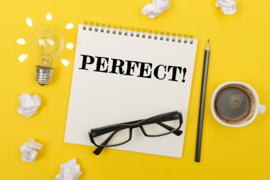 İş ve finans kavramı. Sarı masada: bir ampul - bir fikir, bir fincan kahve, bir parça kağıt, bardaklar ve yazılı bir defter - PERFECT
