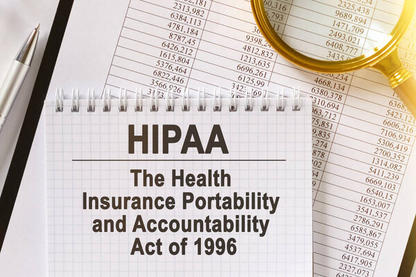 On the table are financial reports, a pen, a magnifying glass and a notebook with the inscription - HIPAA. The Health Insurance Portability And Accountability Act of 1996.