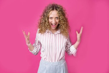 Kıvırcık saçlı bir kadın sevinçten avuçlarını kaldırıyor, birinden inanılmaz bir hediye aldığına seviniyor, yüksek sesle bağırıyor, çizgili bir gömlek giyiyor. Mor bir arka planda izole edilmiş..