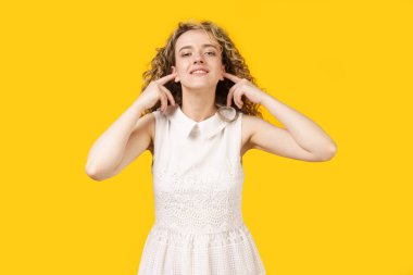 Parmaklarıyla kulaklarını kapatan genç bir kadının portresi. Sarı arkaplanda izole edilmiş